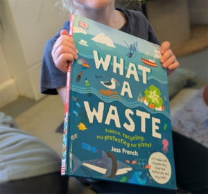 A child at Spring RAF Halton holding a book titled "What is waste?" helping educate the children on recycling.